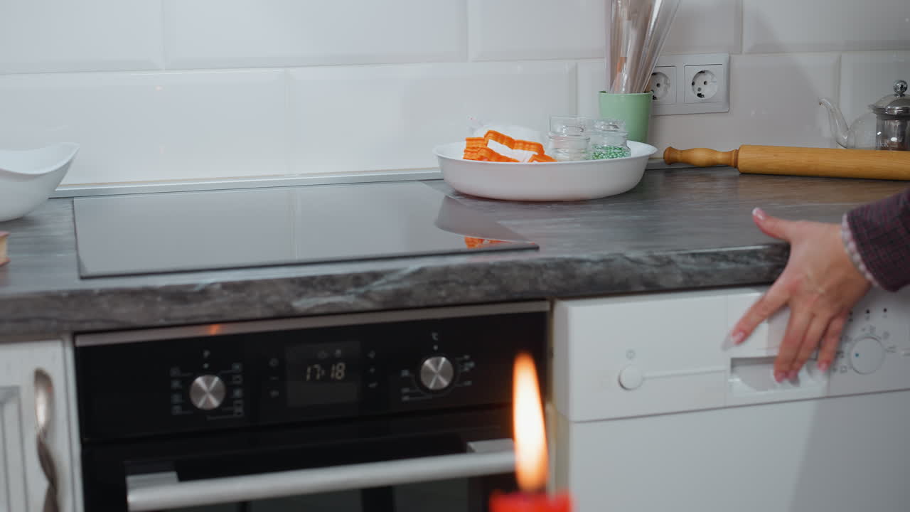 Visuale parziale di una persona che rimuove una pentola da un mobile della cucina per posizionarla su un elegante piano cottura elettrico con display digitale; la moderna cucina presenta una lavastoviglie aperta ed elementi da piano di lavoro