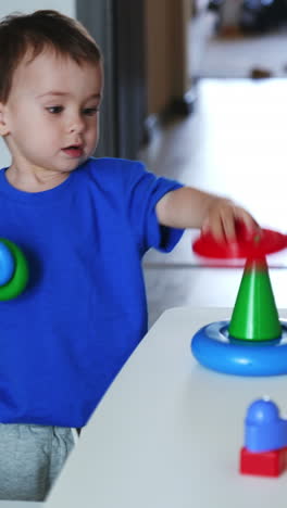 baby boy in blue t-shirt assembles toy pyramid. kid plays with a toy and drops it on the floor. vertical video