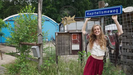 Schöne-Frau,-Umweltbewusster-Hippie,-Der-An-Einem-Antikapitalistischen-Straßenschild-Festhält-Und-Es-Ansieht-Und-Sagt:-Kapitalismus-Weg,-Weg-Mit-Dem-Kapitalismus,-Postkapitalismus,-Zurück-Zu-Den-Grundlagen-In-Der-Natur,-Netzunabhängiges-Leben