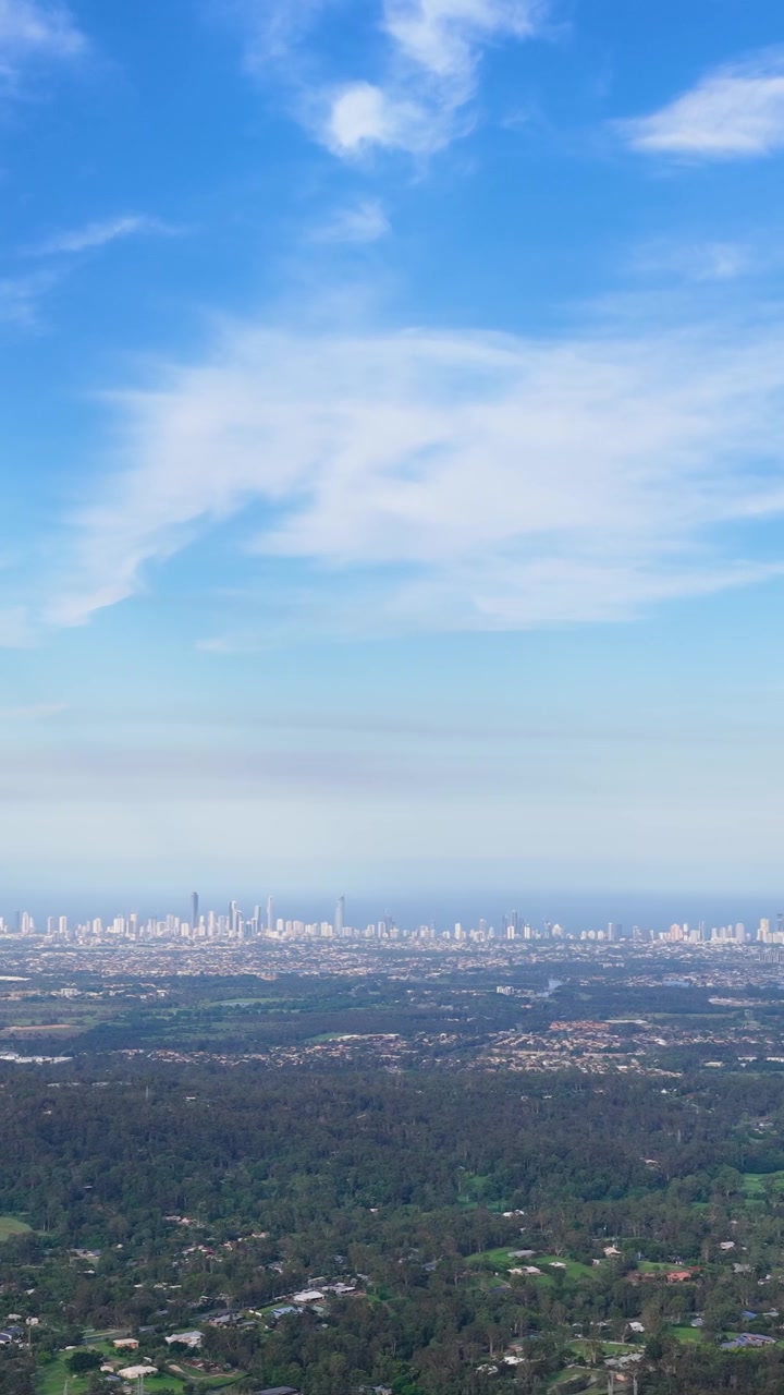 Cámara aérea panea desde el interior para revelar el horizonte de una ciudad costera bajo un cielo azul brillante.