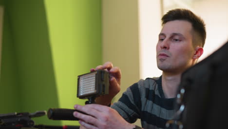 studio guy adjusting led video light in home studio setup. focus on hand holding light. background features green wall and soft indoor lighting, creating a cinematic environment