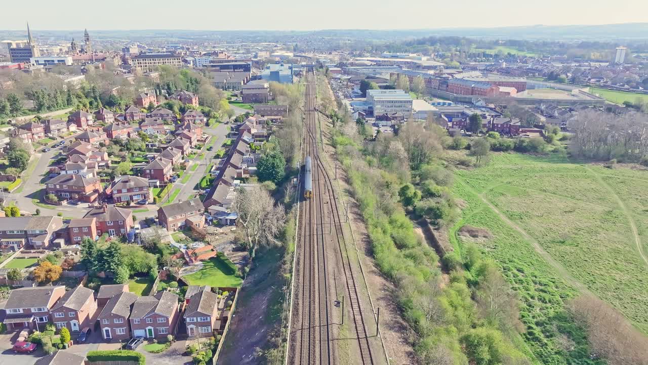 Aerial view of Wakefield, England, with a high-speed train centre framed, passing through traditional British brick homes, green spaces, and industrial areas in the suburban landscape