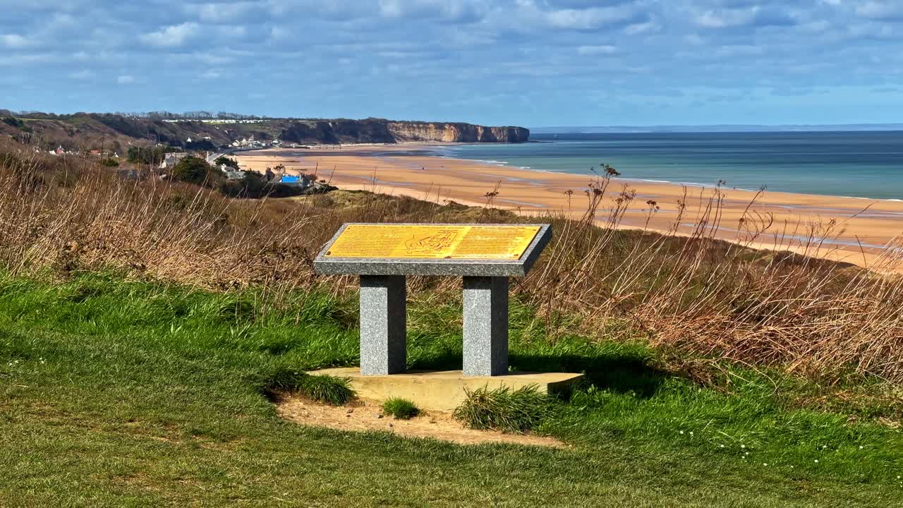 Un cartello storico si erge sopra Omaha Beach, offrendo ampie vedute della costa e delle scogliere.