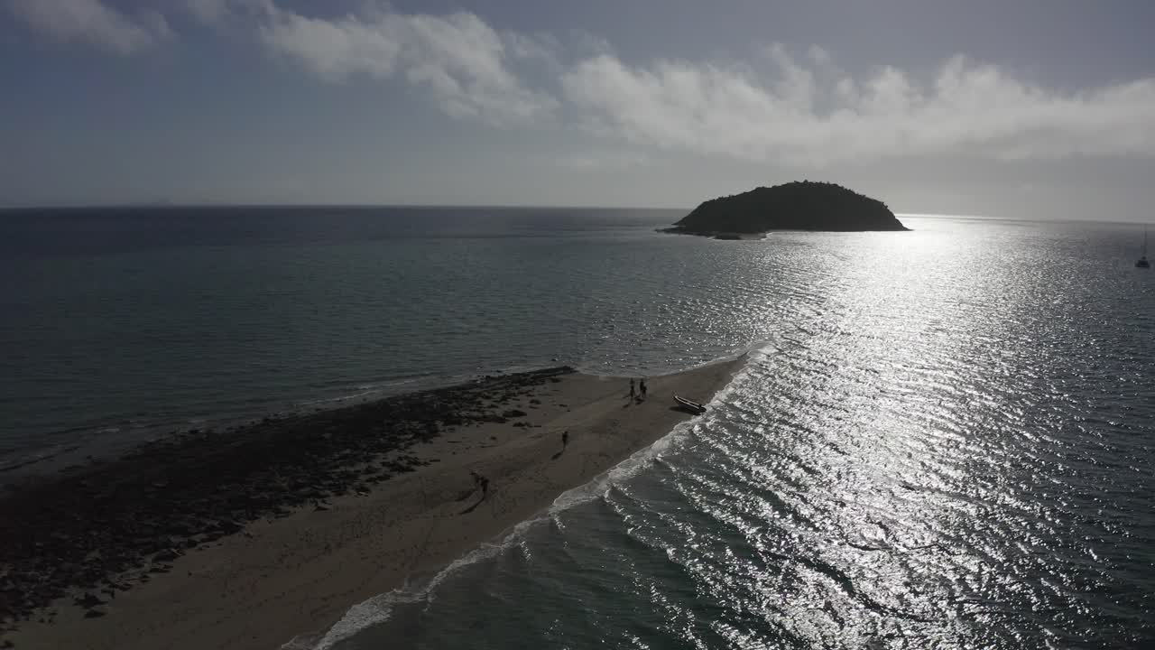 Inflatable boat on tiny beach spit with afternoon sun beam on ocean