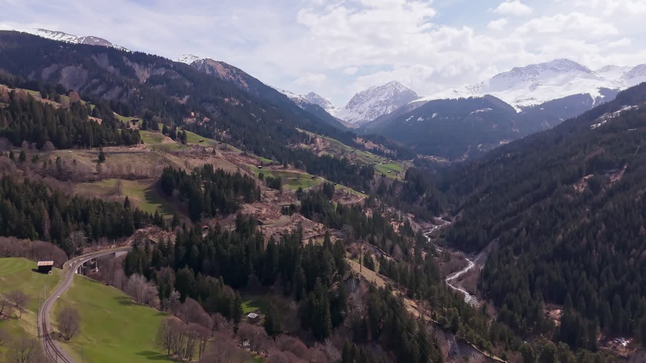 Lush green valleys, winding river, and snow-capped mountains in peist, switzerland, aerial view