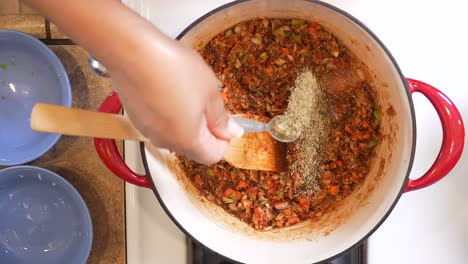 adding thyme to the roux gumbo mixture as it simmers in a pot on the stove - overhead view in slow motion gumbo series