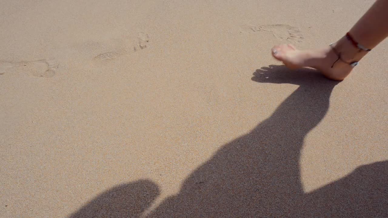 A traveler tourist girl walks on the beach while leaving her footsteps behind on the sand. After she goes out of frame, a wave from the sea drags a watermelon husk contaminating the beach