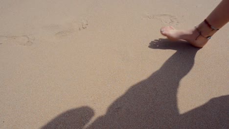 a traveler tourist girl walks on the beach while leaving her footsteps behind on the sand. after she goes out of frame, a wave from the sea drags a watermelon husk contaminating the beach