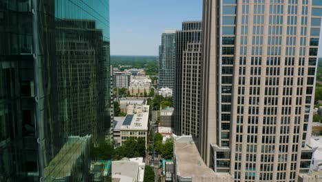 drone flies between buildings in urban city with green trees and forest in the distance