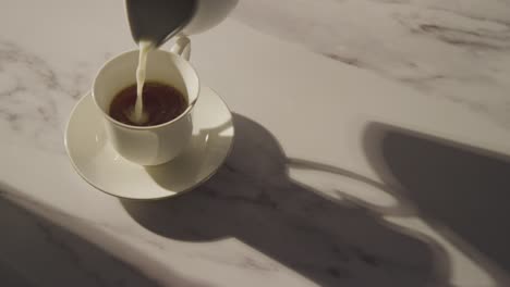 studio shot of person adding milk to traditional british cup of tea using teapot 2