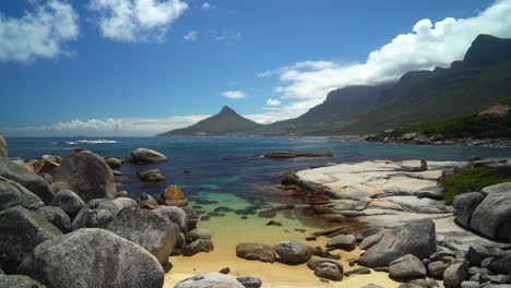 épica impresionante ciudad del cabo playa kommetjie roca arena blanca profunda agua azul vista panorámica leones cabeza mesa montaña medio día polarizado agua clara sur de áfrica cinematográfica cámara lenta panorámica a la izquierda