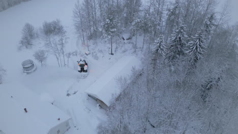 Tractor-plowing-snow-for-forest-home-in-Arctic-winter-landscape,-aerial-view