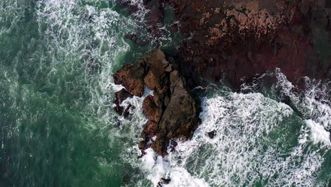 Foamy-sea-waves-crashing-upon-rugged-coastline-with-sharp-rocks