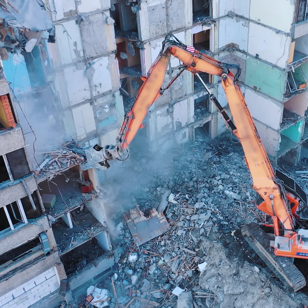 Dismantling of a high bulding. Excavator demolishing ruins for new construction project. Flying above a destruction
