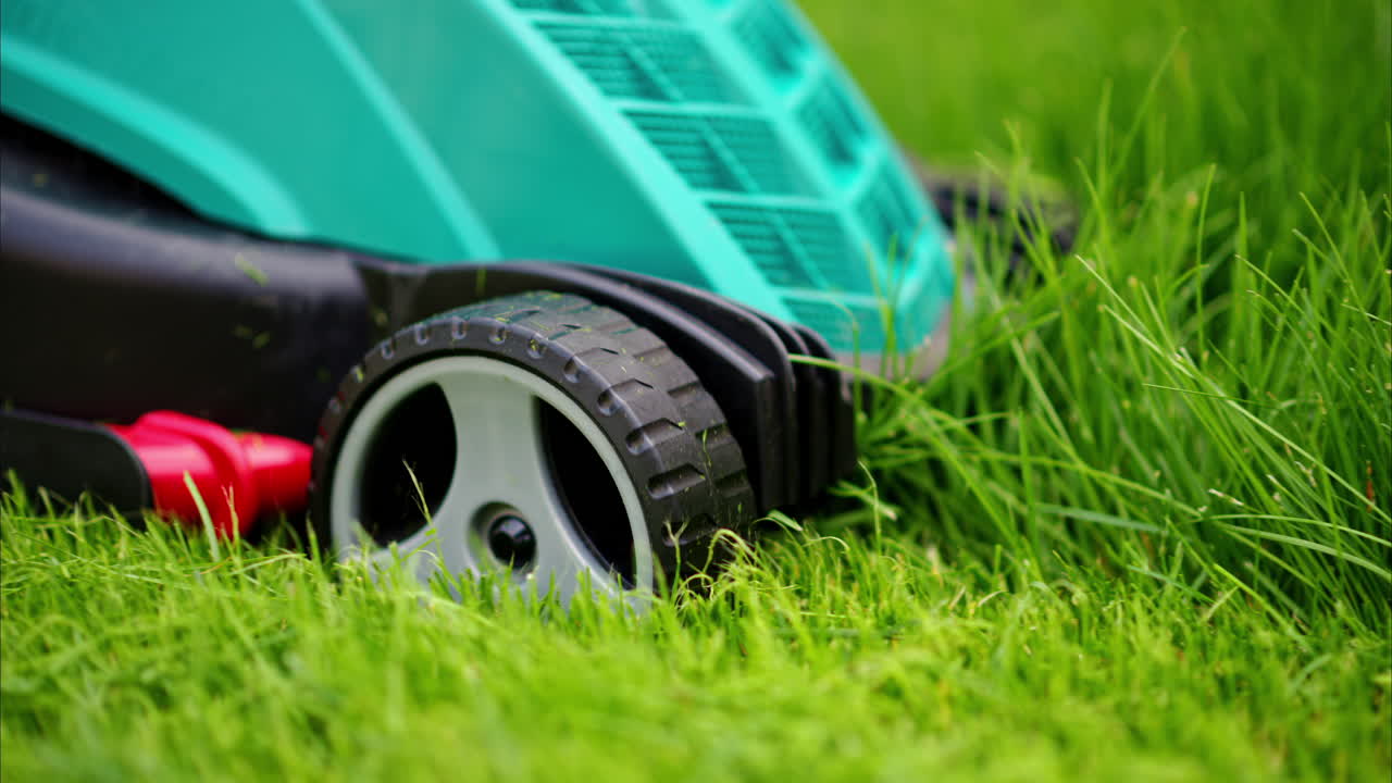 Close up of turquoise lawn mower machine cutting the grass