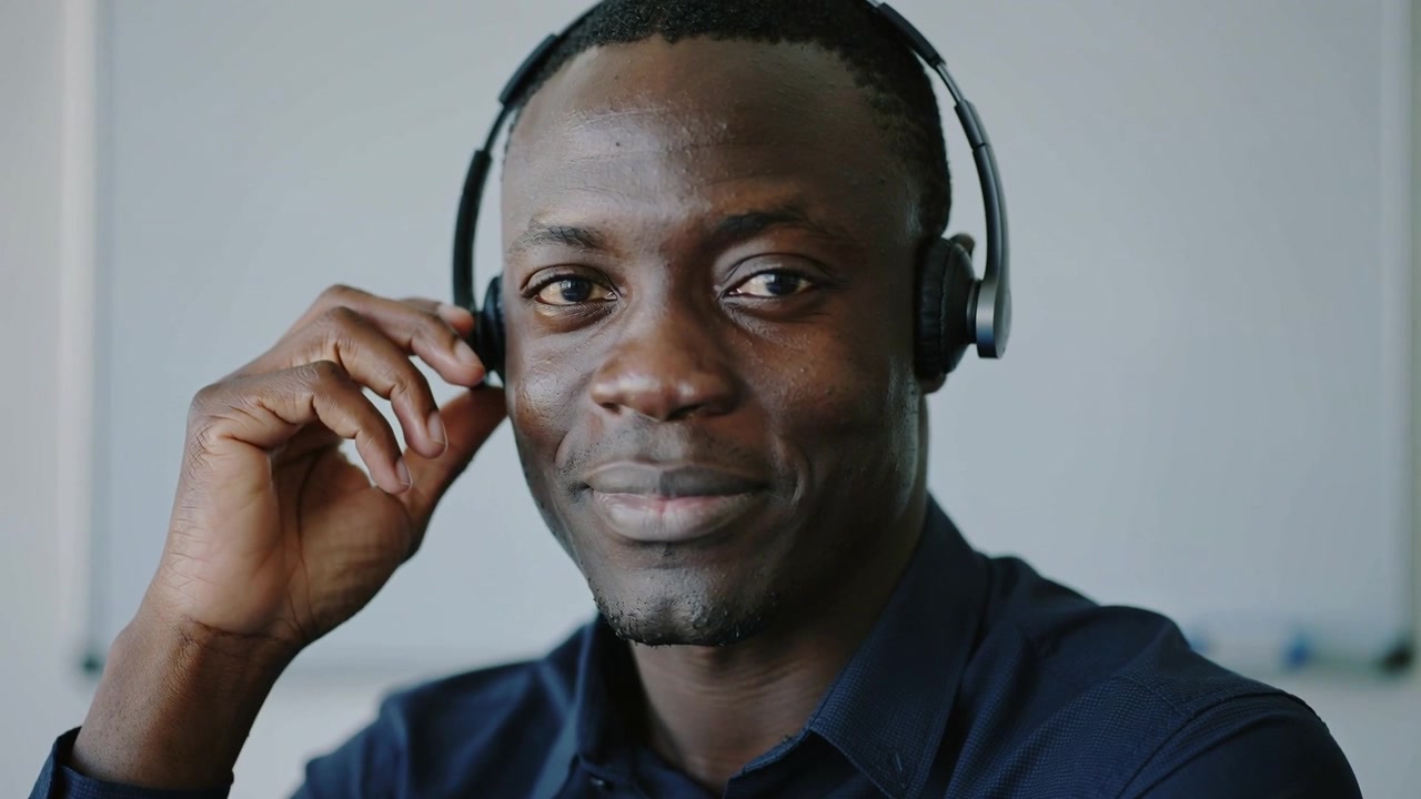 Adjusting adult male in dark collared shirt positioning left ear cup at small office