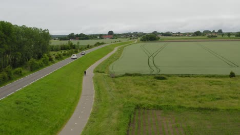 long aerial tracking shot of traffic through agricultural land on the peninsula of walcheren in zeeland, the netherlands, on a cloudy summer day