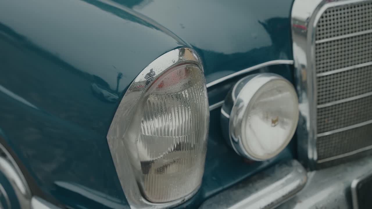 Nahaufnahme der Front eines klassischen blauen Oldtimers mit Chromkühlergrill und runden Scheinwerferdetails