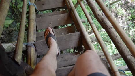 Legs-of-a-man-in-flip-flops-walking-down-wooden-stairs-in-jungle