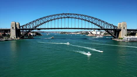drone climbs in front of sydney harbour bridge with sydney opera house in the background on a bright, sunny day