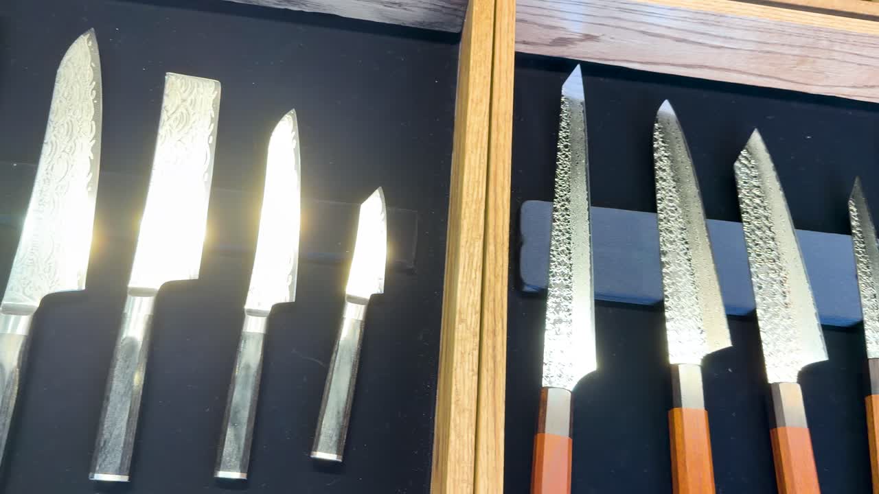 Un lent panoramique de caméra sur des couteaux de cuisine japonais artisanaux aux manches en bois et aux motifs Damas.