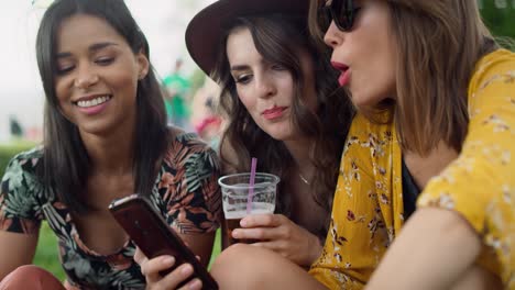 happy women sitting on the grass and using mobile phones