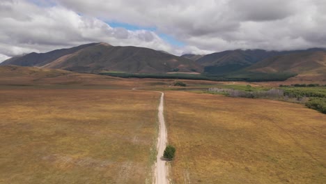 Dirt-road-cuts-through-vast-wild-landscape-toward-mountains---aerial-push-in