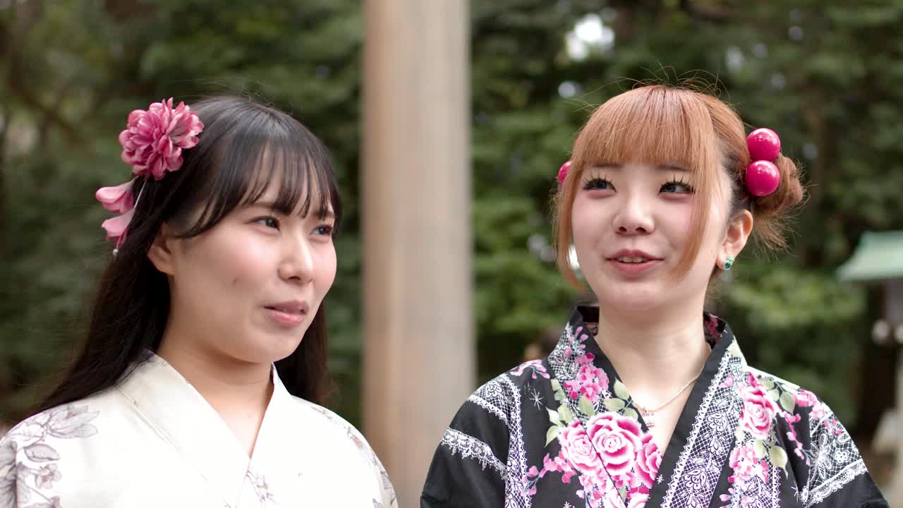 Due donne che indossano yukata floreali sono in piedi all'aperto, parlano e sorridono alla luce naturale del giorno