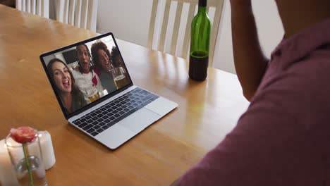 Mixed-race-man-sitting-at-table-using-laptop-making-video-call-with-friends