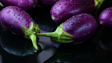 Tilt-down,-Purple-eggplants-covered-with-water-droplets-on-black-background-with-water-reflection