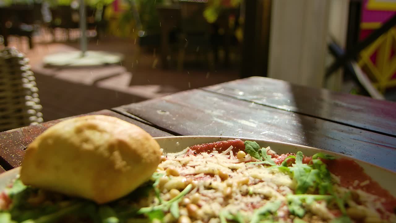 Slow backwards focus rack reveal of pepper flakes falling on plate with carpaccio