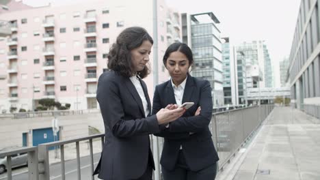 focused businesswomen using smartphone on street