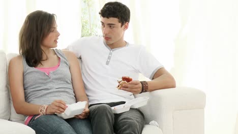 Couple-of-teenagers-eating-burgers-and-talking-on-the-sofa