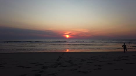 Surfer-walking-on-the-beach-with-a-beautiful-sunset