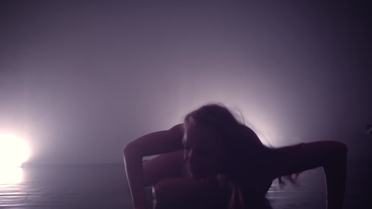Silhouette of a young woman performing modern dance moves moves on a stage with spotlight in the background