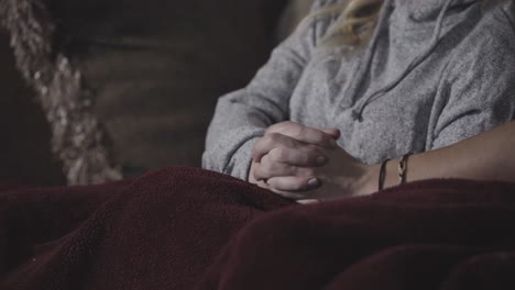 a young couple watching tv holds hands while cuddling under a blanket together