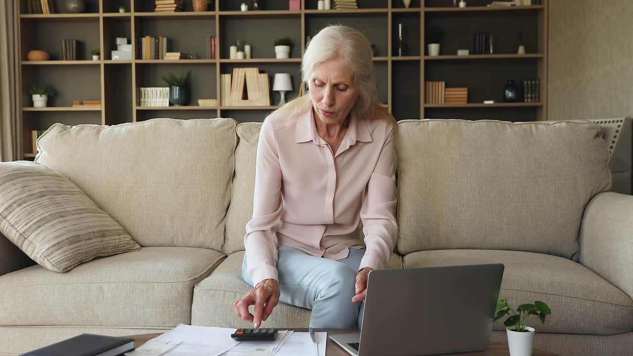 пожилая женщина рассчитывает расходы, использует калькулятор, оплачивает счета через электронный банк.