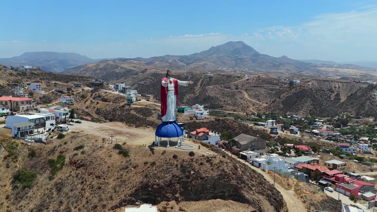 Flygfoto i närbild av statyn Kristus av det heliga hjärtat (Cristo del Sagrado Corazón) i Rosarito, Baja California, Mexiko, omgiven av bostäder i ett bostadsområde