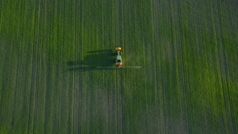 Vista-Aérea-De-Un-Agricultor-Rociando-Campos-De-Cultivo-Con-Tractor,-Rociando-Pesticidas-Y-Fertilizantes,-Tarde-Soleada-De-Verano,-Luz-De-La-Hora-Dorada,-Amplio-Tiro-Ascendente-De-Drones-De-Ojo-De-Pájaro-Avanzando