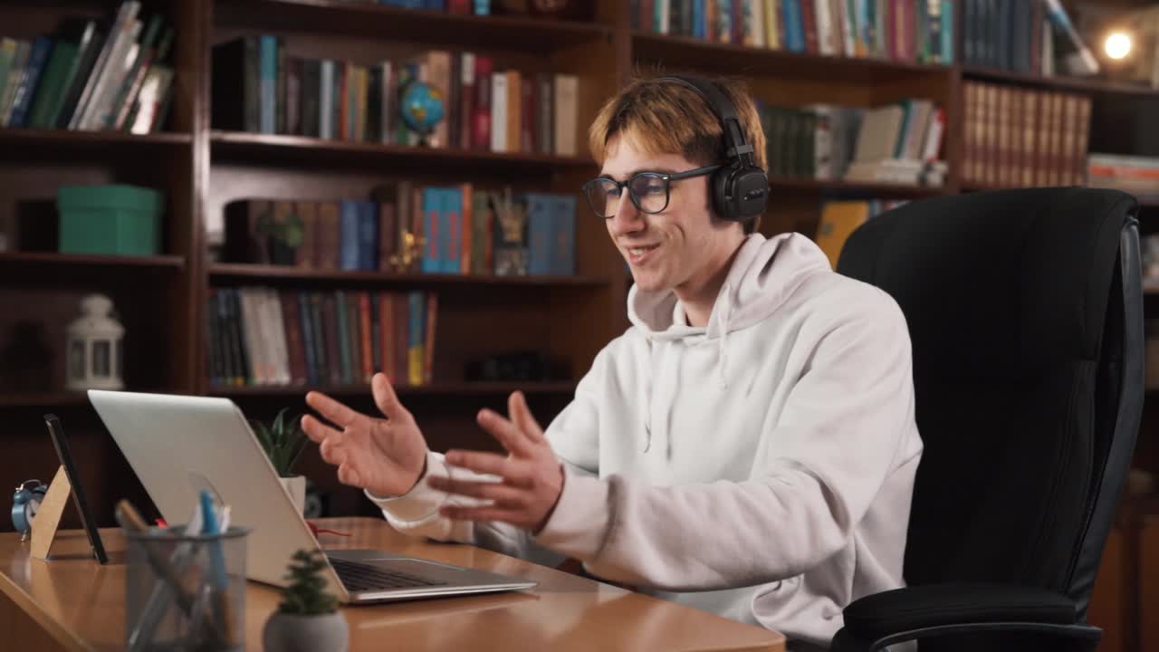 The guy is sitting behind a laptop, engaged in a video call with someone