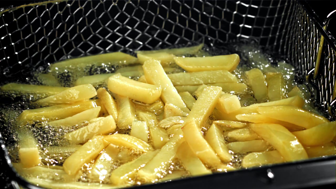 Patatine fritte dorate che cuociono in olio bollente e frizzante