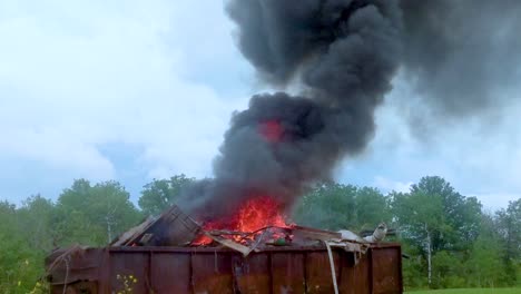 Dicker-Dunkler-Rauch,-Der-Aus-Einem-Brennenden-Müllcontainer-Voller-Müll-Auf-Ländlichem-Ackerland-Aufsteigt