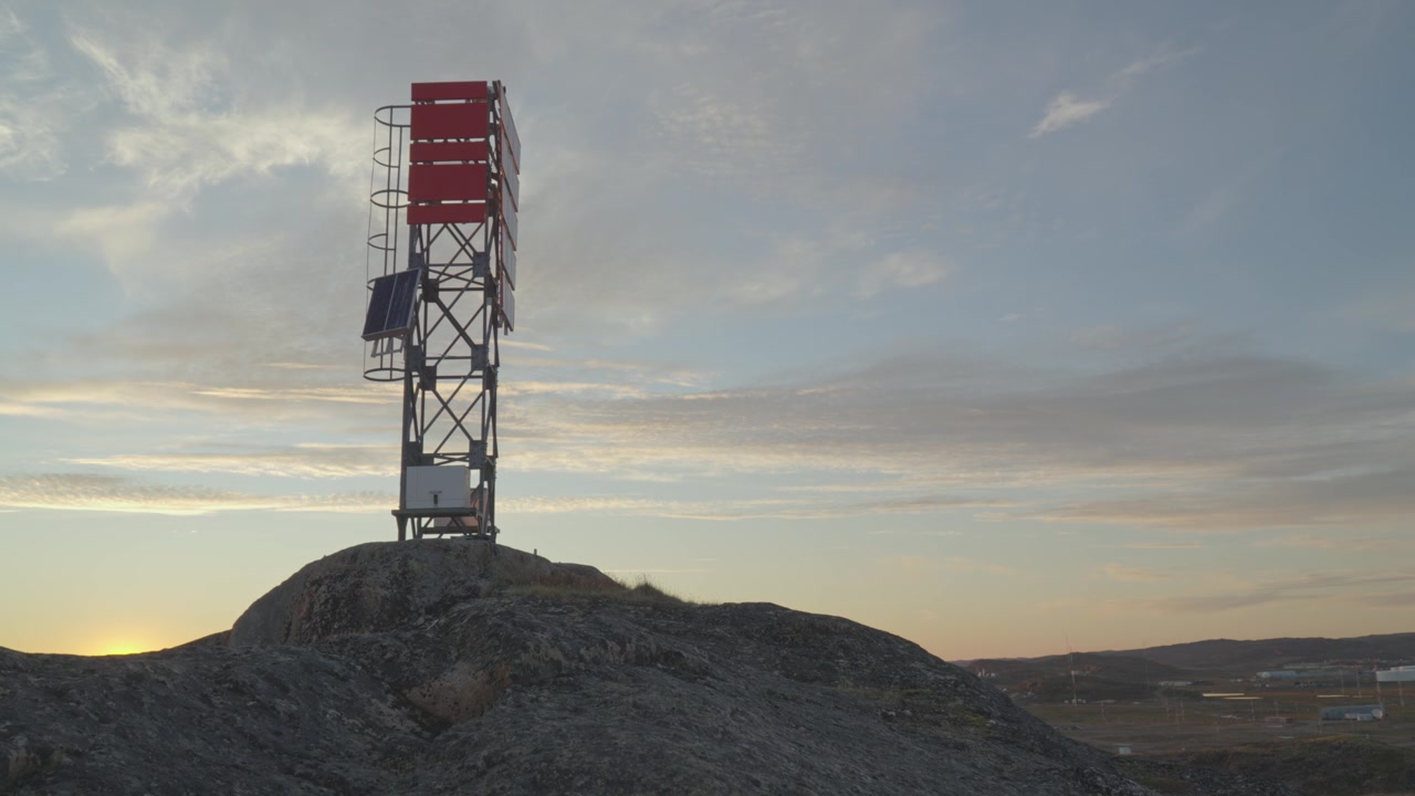Lavvinkelbillede med fokus på et rød-hvidt navigationsvarselstårn og en kommunikationsmast, der står på et blotlagt granitfremspring over byen