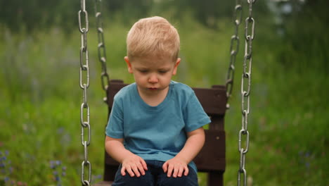 Upset-little-boy-kid-sits-on-swings-on-ground-at-countryside