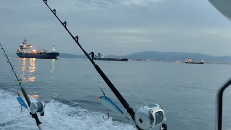 Blick-Auf-Das-Fischerboot-Mit-Zwei-Auf-Rutenhaltern-Montierten-Angelruten,-Das-In-Den-Gewässern-Der-Straße-Von-Gibraltar-Schwimmt,-Und-Die-Fracht--Oder-Kreuzfahrtschiffe-Im-Hintergrund