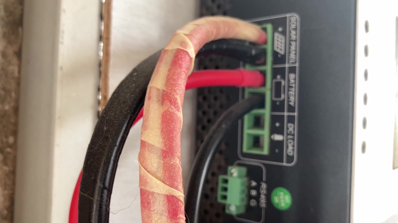 Handheld 4K close-up, selective focus on red and black cables connecting solar panel installation to a generic MPPT solar charge controller. Highlights wiring and renewable energy DIY setup.