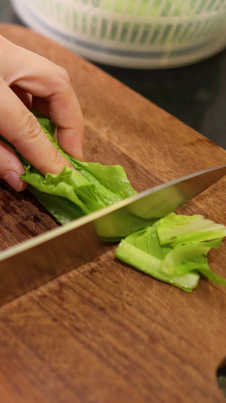 Primo piano di una mano che taglia lattuga fresca su un tagliere di legno