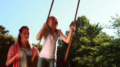 little girl being pushed on a swing by her mother in the park