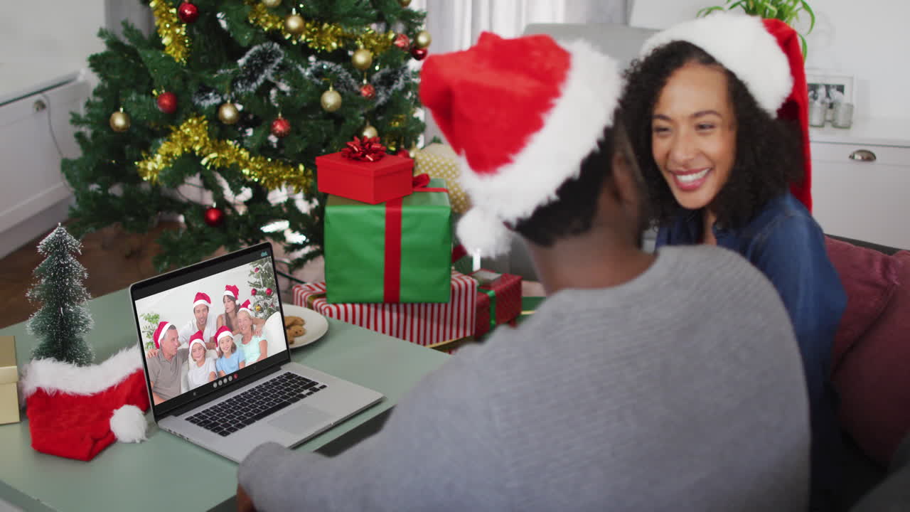 pareja afroamericana con sombreros de santa haciendo una videollamada en una computadora portátil en casa durante la navidad
