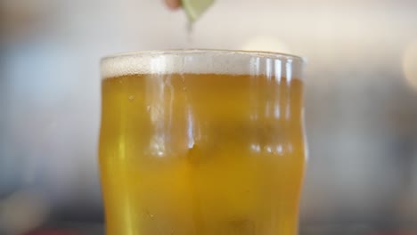 chef squeezing a lime into a beer, then dropping it intothe beer as camera pans down